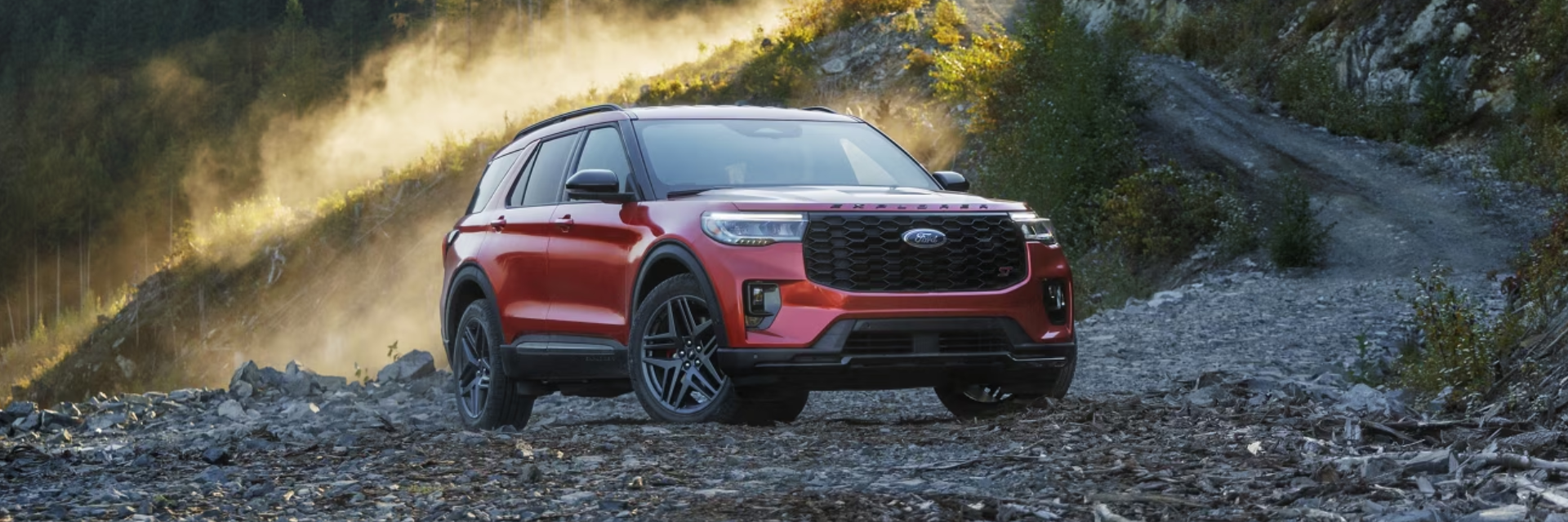 A sleek white 2025 Ford Explorer driving on a scenic mountain road, showcasing its dynamic design and premium features. The SUV features bold mesh grille, signature lighting, and 21-inch magnetite painted wheels, highlighting its sophistication and flair.
