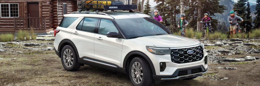 A sleek white 2025 Ford Explorer driving on a scenic mountain road, showcasing its dynamic design and premium features. The SUV features bold mesh grille, signature lighting, and 21-inch magnetite painted wheels, highlighting its sophistication and flair.